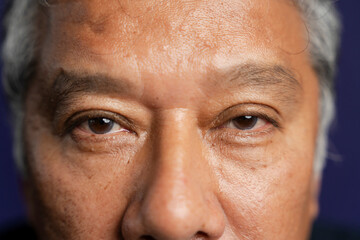 Close-up of senior man looking at camera against purple background