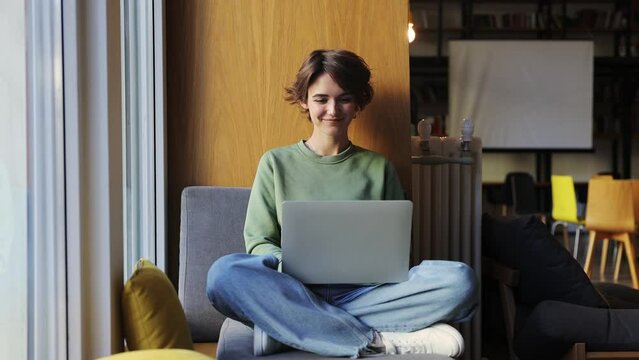Young girl college student wear green clothes sit in chair use pc laptop computer watching distance online learning seminar class remote university webinar having virtual classroom meeting in library