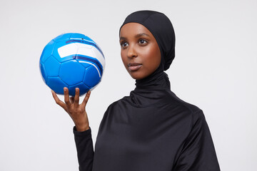 Studio shot of young woman in hijab holding soccer ball