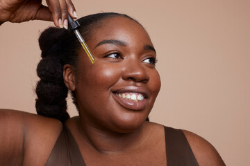 Studio shot of smiling young woman applying face serum