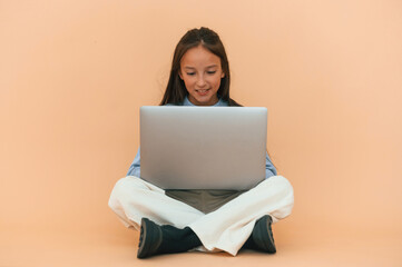 Using laptop, sitting. Cute young girl is in the studio against background