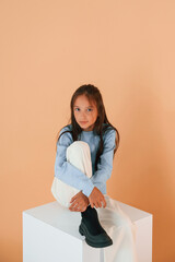 Sitting on white cube. Cute young girl is in the studio against background
