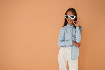 In stylish glasses. Cute young girl is in the studio against background