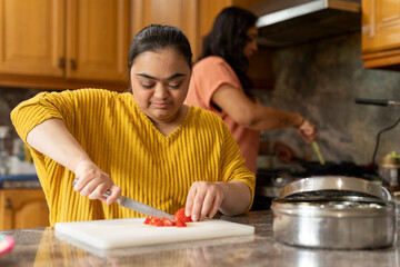 Woman with down syndrome preparing food with mother in kitchen - obrazy, fototapety, plakaty