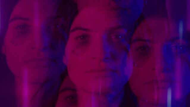 Young sad woman with smudged mascara staring at camera, posing in a dark studio with colorful neon light. Kaleidoscope effect, video portrait