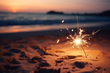 Fototapeten Glowing sparkler in the sand by the seashore in the moonlight with a softly blurred background in pink and orange colors.A warm and festive atmosphere of holiday even © Nataliya