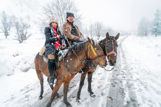Asian tourist horse riding to see scenery of Sonmarg Valley in Himalayas during winter Christmas trip, honeymoon vacation, romantic journey. Weather white and snowing. Sonamarg, Jammu, Kashmir, India