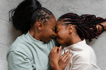 Directly above view of lesbian couple embracing while lying on carpet - obrazy, fototapety, plakaty