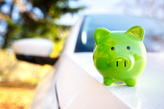 Green piggy bank money box on top of car hood, new vehicle purchase, insurance or driving and motoring cost