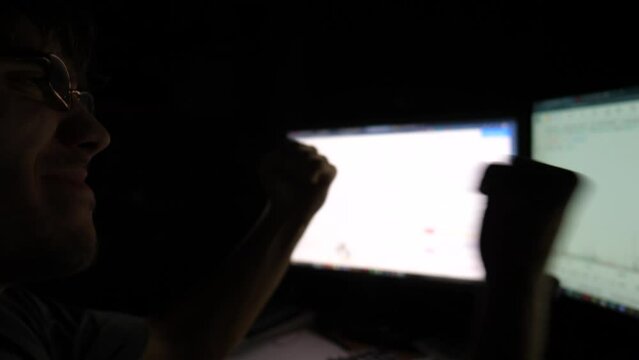 Young financial analyst works on computer and happy for success. Smiling stock market broker celebrating good news. Concept of bitcoin BTC and stock market or crypto trading online. Smiling freelancer