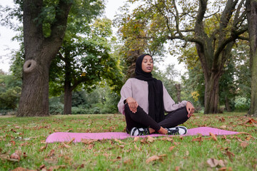 Woman in hijab meditating in park