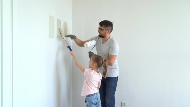 Happy family, father and little daughter choose wall paint on test of different colors at home in apartment. Repair concept