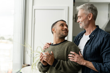 Mature male couple standing by window at home