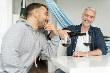Fototapeta na wymiar Male couple pouring red wine at home