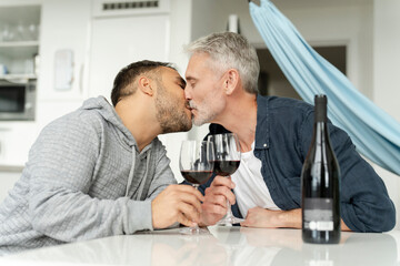 Male couple drinking red wine and kissing at home