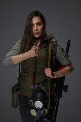 Fototapeta na wymiar Middle Eastern descent in post-apocalyptic survival gear, brandishing a dagger on a gray backdrop, showcasing her determination to survive