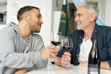 Male couple raising toast with red wine at home