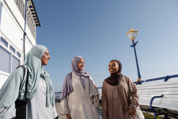 Three Muslim women standing on pier on sunny day
