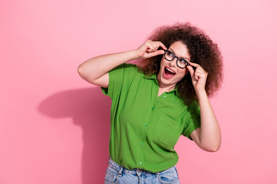 Photo portrait of attractive young woman touch specs look empty space dressed stylish green clothes isolated on pink color background