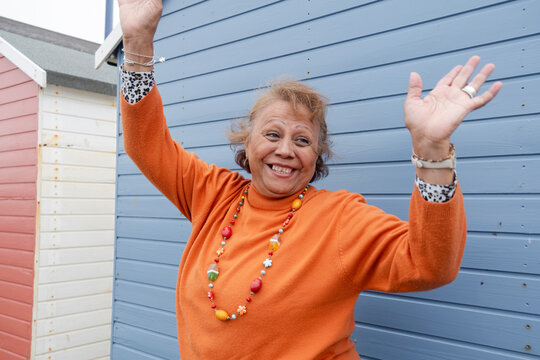 Portrait of smiling senior woman with hands raised against blue hut - Powered by Adobe