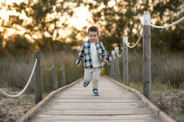 Niño con camisa de cuadros paseando sobre un puente rodeado de naturaleza - obrazy, fototapety, plakaty