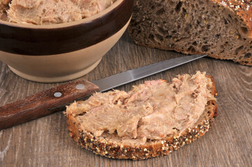 Tranche de pain aux graines avec des rillettes et un couteau en gros plan.