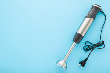 New hand blender with black wire on blue table background. Pastel color. Closeup. Kitchen...