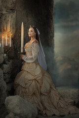A beautiful red-haired girl in an old medieval dress with swords stands in the mountains and looks into the distance. Fairytale story about a princess. magic light. Warm artistic work. © olenakucher