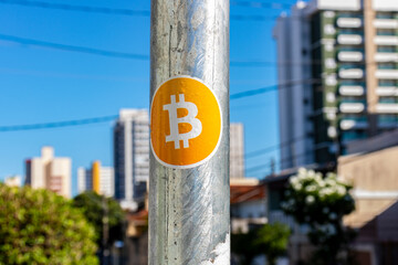 Bitcoin symbol, glued to a metal pole, with a city landscape in the background. Finance, economy,...