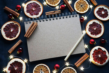 Notepad with pen next to dry fruit slices, Christmas tree decorations, cinnamon sticks on a dark...