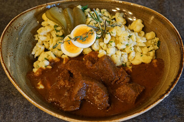 Close up Austrian beef Goulash steak served with pickled cucumber, hashed egg and Spätzle or Knöpfle(type of pasta made with fresh eggs)