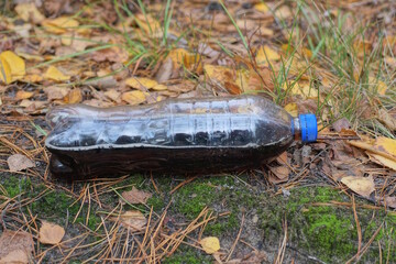one plastic bottle with a black drink lemonade lies on the ground and green moss on the street in nature