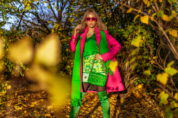 Beautiful woman wearing a pink elegant coat and green scarf is posing outdoors on a sunny autumn day.