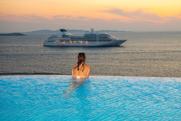 Woman enjoys at infinity pool at the sunset time, Mykonos, Greece