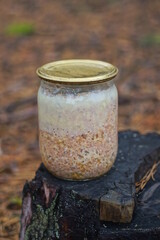 Naklejka premium one glass jar with brown chicken stew standing on a stump on the street