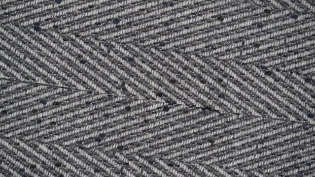 closeup rotation of tweed woolen herringbone fabric. rough texture of natural wool fabric with a classic white gray pattern.