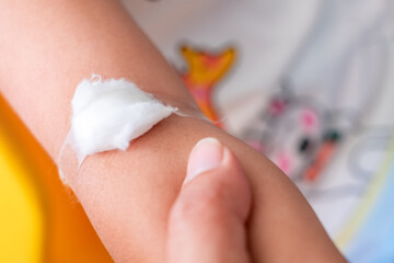 Close up of mother holding hand's girl with plaster are placed on the child's arm after vaccination.