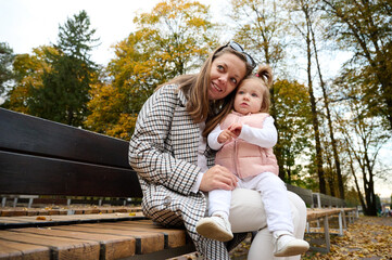 Mother and cute baby girl walking in autumn park with leaves on the ground. Mom spending time with...