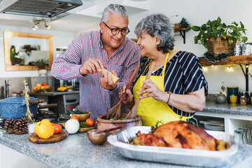 Latin senior couple cooking a turkey meat together for Christmas dinner at home in Mexico Latin America, hispanic people preparing food in holidays