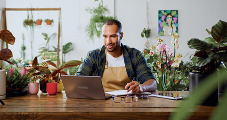 Caucasian man florist using laptop, typing and taking inventory in Plant Store. Botanist working, small business owner. Florist working on computer at workplace.