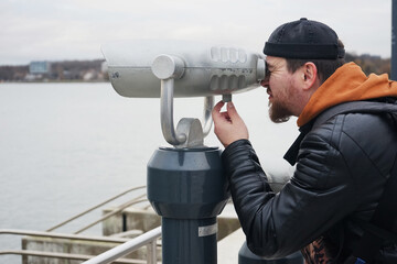 Obraz premium A man in a docker's cap looks at the binocular viewer on the sea promenade
