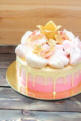 Gradient pink birthday cake with meringue clouds, chocolate stars, donuts and golden fondant crown for a little princess. Rustic wooden background