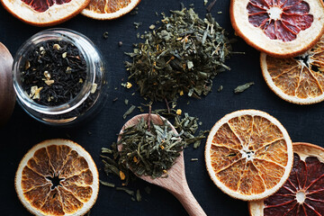Loose leaf tea in a wooden spoon next to tea and dry citrus slices
