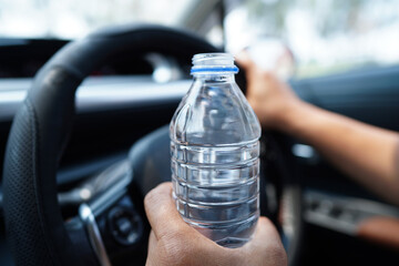 Asian woman driver hold cold water for drink in car, dangerous and risk an accident.