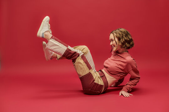 self-expression, joyful woman in patchwork pants and cropped long sleeve sitting on red backdrop - Powered by Adobe