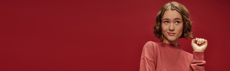 portrait of young pensive woman with short wavy hair looking away on red background, banner