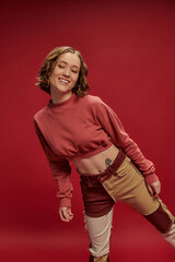 personal style, young happy girl in patchwork pants and cropped long sleeve posing on red backdrop