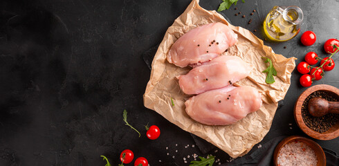 Raw chicken breast meat and spices for its preparation on a black background, top view, web banner with free space for text