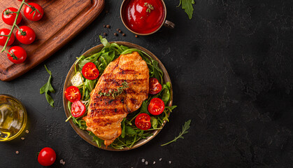 Grilled chicken breast with arugula and tomatoes on a plate, top view, black background with copy...