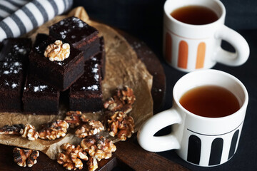 Chocolate cake with walnuts on a wooden board next to cups of tea on a dark background